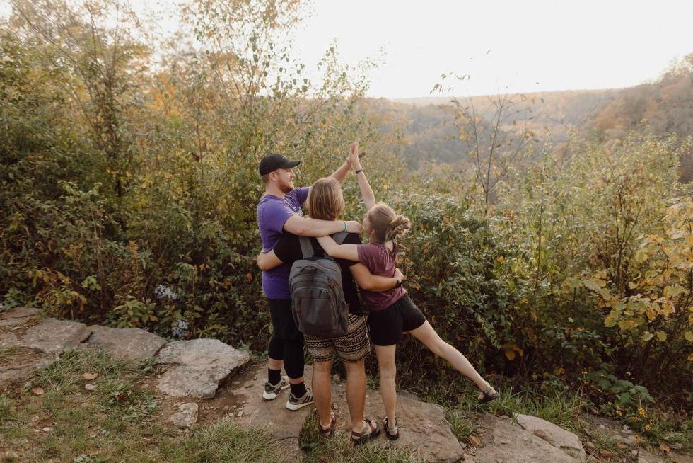 3 Asbury University Students on a hike overlooking a forest landscape hugging and high fiving