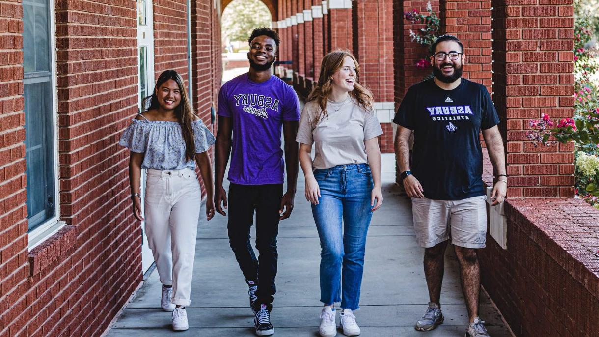4 Asbury University students smile while walking down a path on campus
