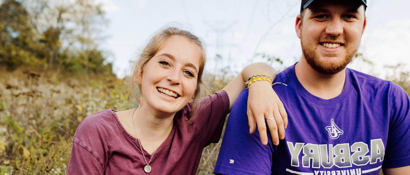 Two Asbury Students sitting in a field smiling for a photo