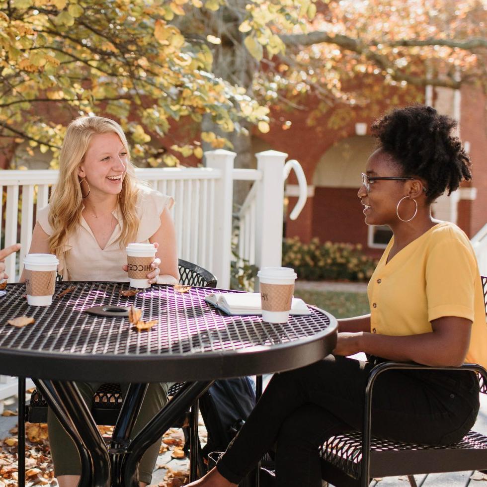 澳门威尼斯人(艾斯拜瑞大学市)校园里的学生们坐在桌子旁愉快地与朋友聊天，桌子上放着咖啡杯.