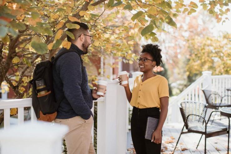 澳门威尼斯人(艾斯拜瑞大学市)的一名准学生站在户外平台上喝着咖啡，在校园参观中与一名指导老师交谈