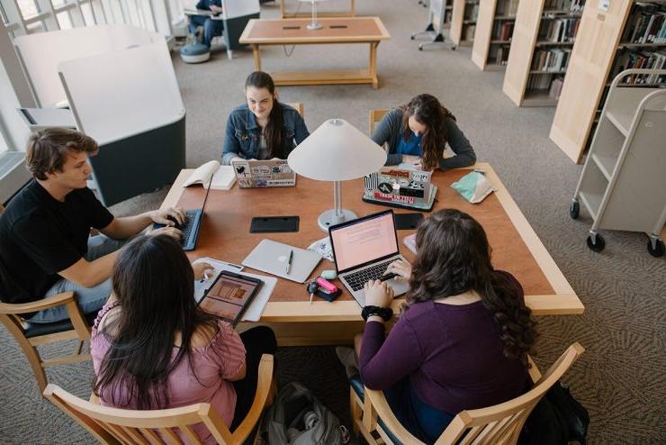 五个澳门威尼斯人的学生围坐在图书馆的桌子旁，拿出了他们的笔记本电脑