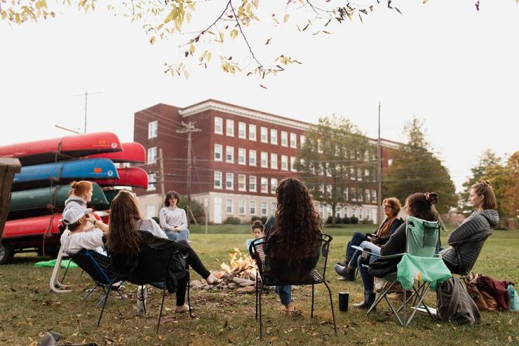 Nine Asbury University students sit around a fire outdoors during the daytime