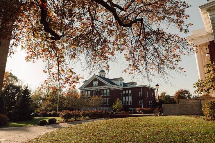 Landscape shot of Asbury University campus in fall with tree branch in front and leaves on the ground